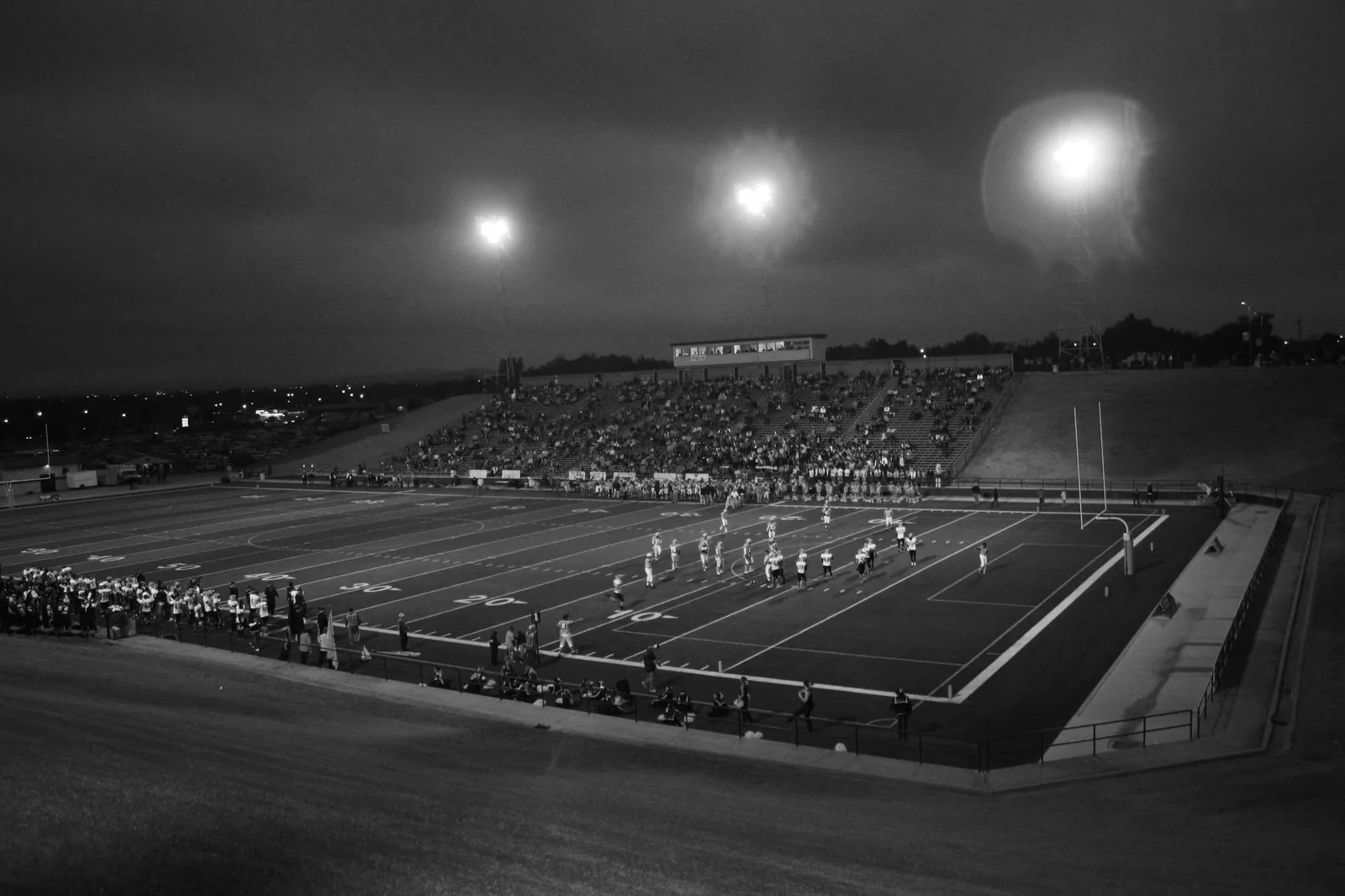 Players line up under the stadium lights at a high school football game.