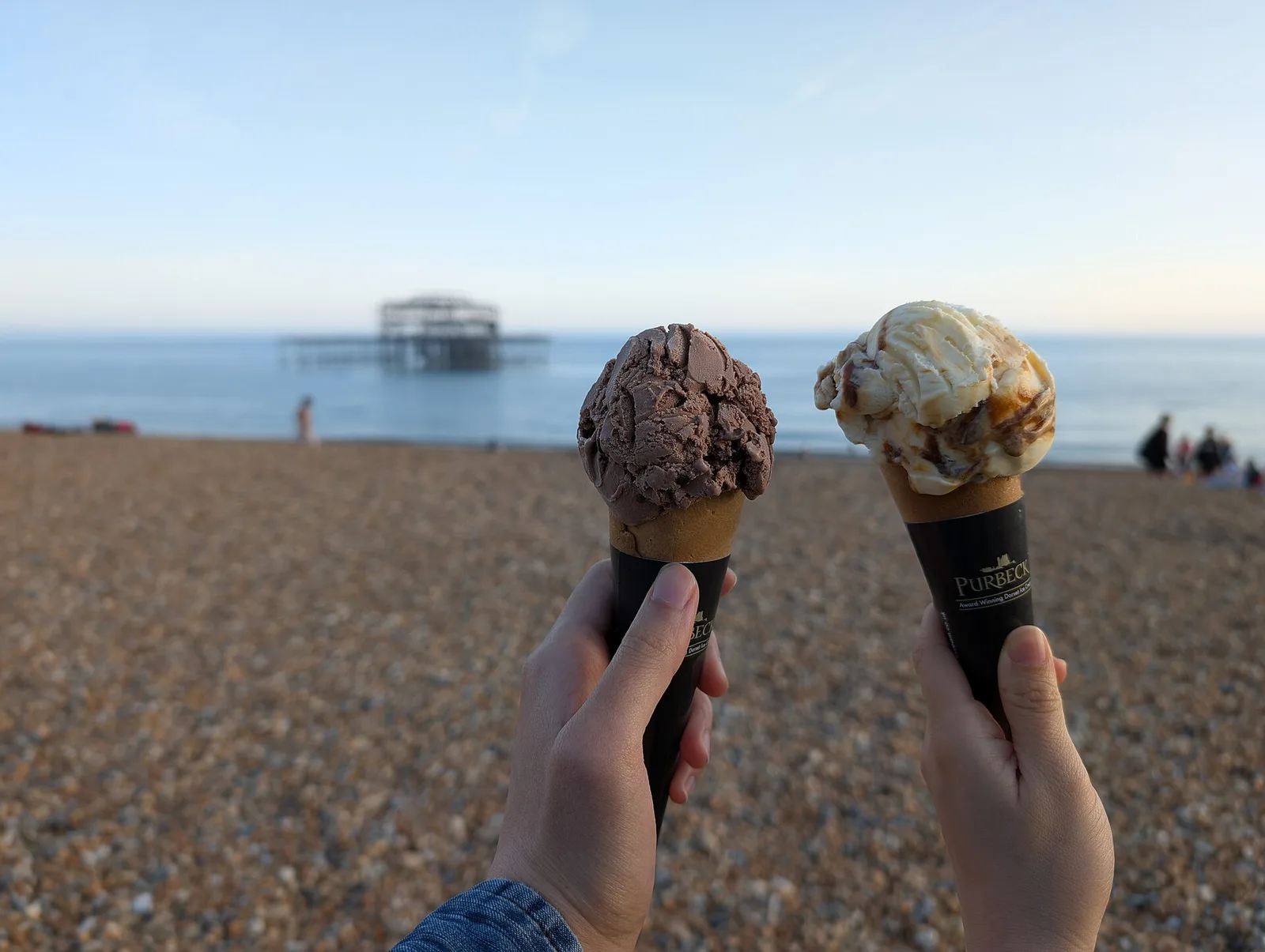Two ice cream cones held up outdoors on a sunny day.