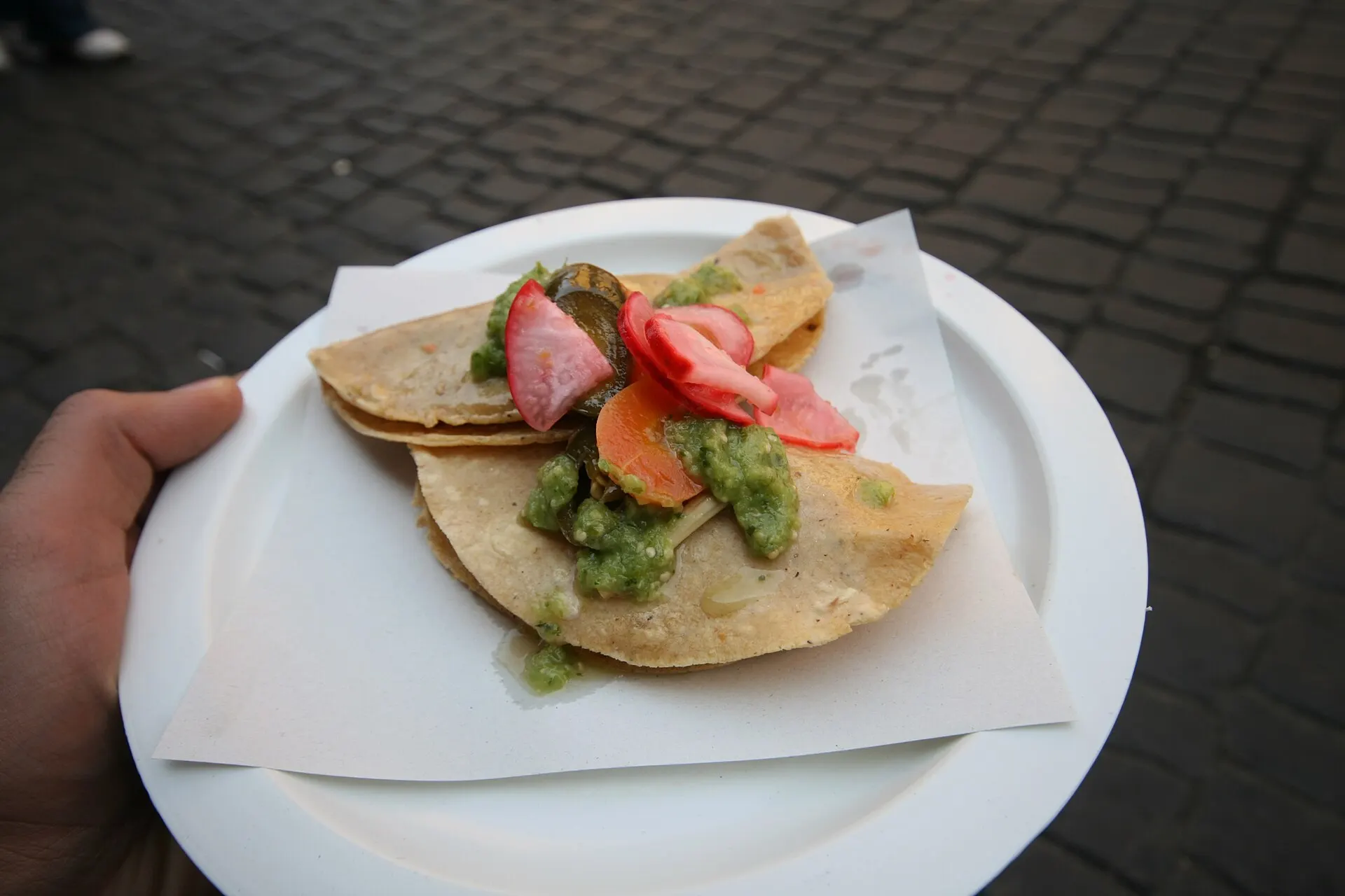 A bean taco and a potato taco topped with green salsa, pickled jalapenos, carrots and radishes, from a street stand in Oaxaca, Mexico.