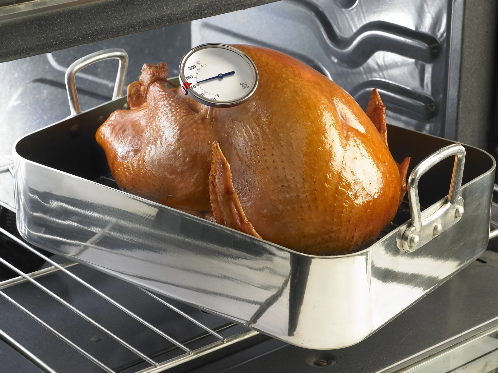 A meat thermometer checks the temperature of a turkey roasting in an oven.