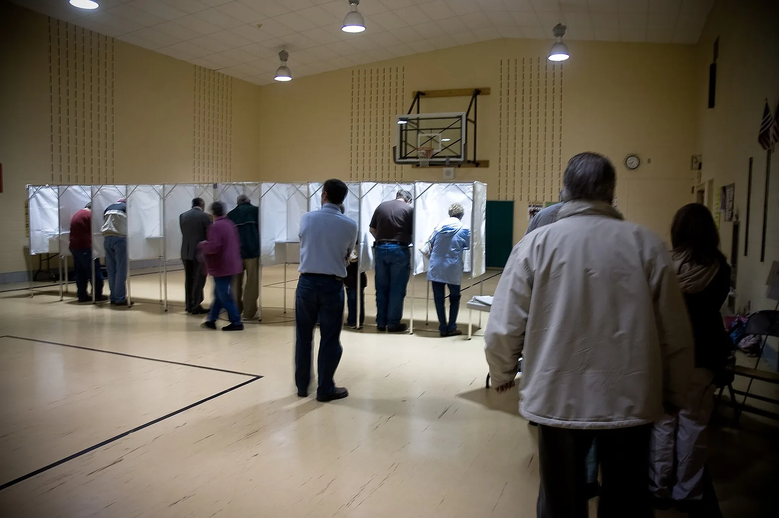 Voters mark ballots in curtained booths at a polling place set up in a school gym.